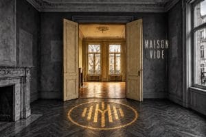 Maison Vide - an empty grey room, its double doors open on a golden lit room